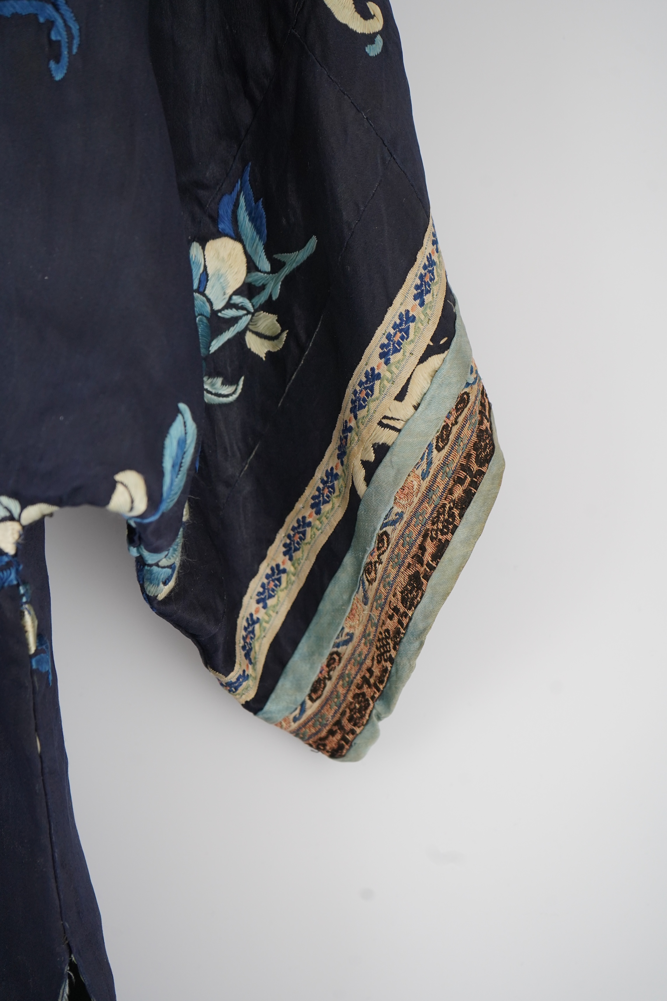 An early 20th century blue silk embroidered Chinese child’s robe, embroidered with bats and flower motifs, bordered with rows of silk braid. Condition - the original silk lining has been removed, it may benefit from bein